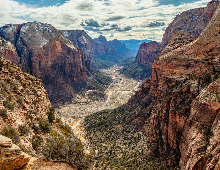 A broad canyon between red cliffs, with a winding river and patches of green below.
