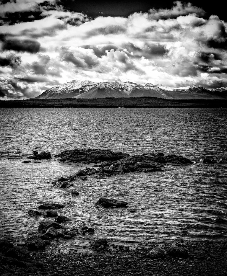 Black-and-white photograph of a rocky shoreline and open water beneath dramatic clouds.