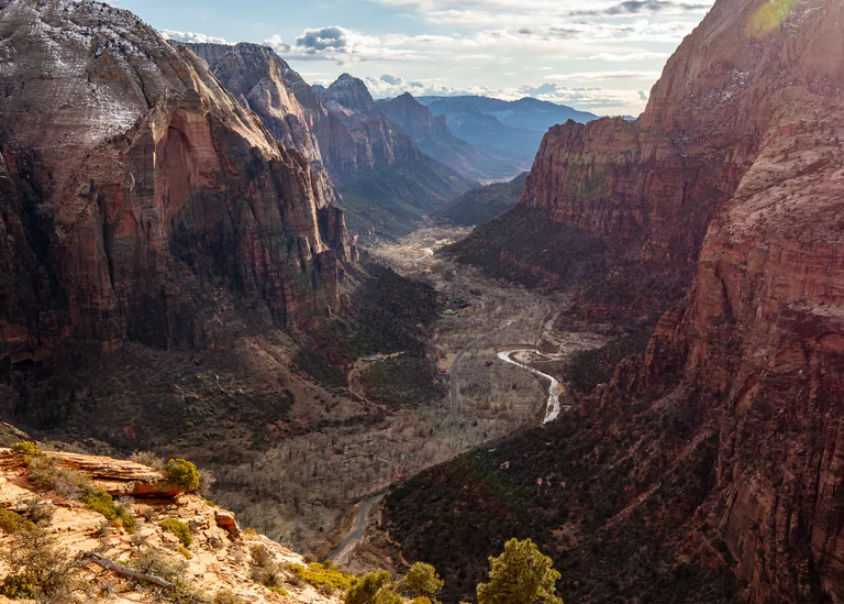 A wide canyon valley with a winding river seen from high between red cliffs.