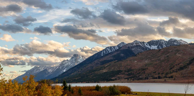 A mountain lake lies beneath a long snowy ridge and layered gray clouds.