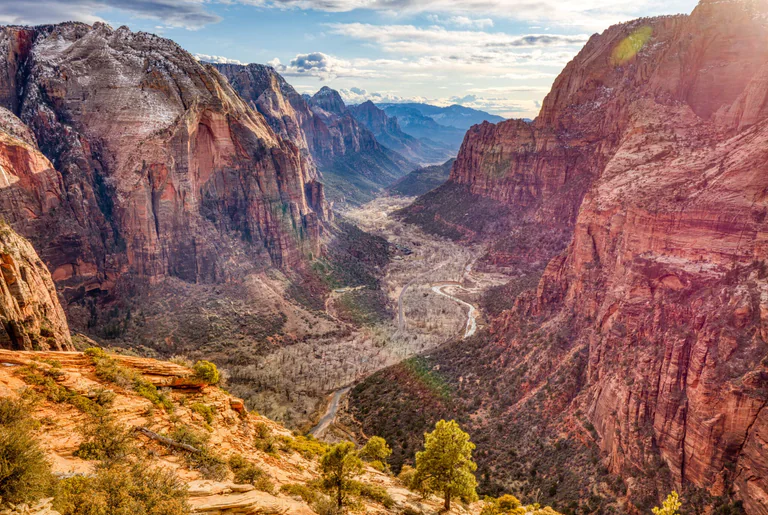 A high view along a green canyon floor between towering red cliffs at Angels Landing.