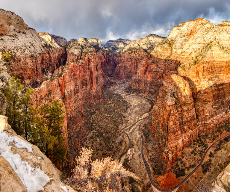 Wide view of rugged red and pale cliffs above a forested canyon at Angels Landing.