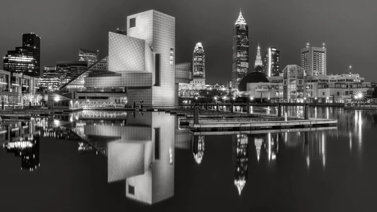 Black-and-white view of Cleveland’s waterfront and the Rock and Roll Hall of Fame reflected in still water.