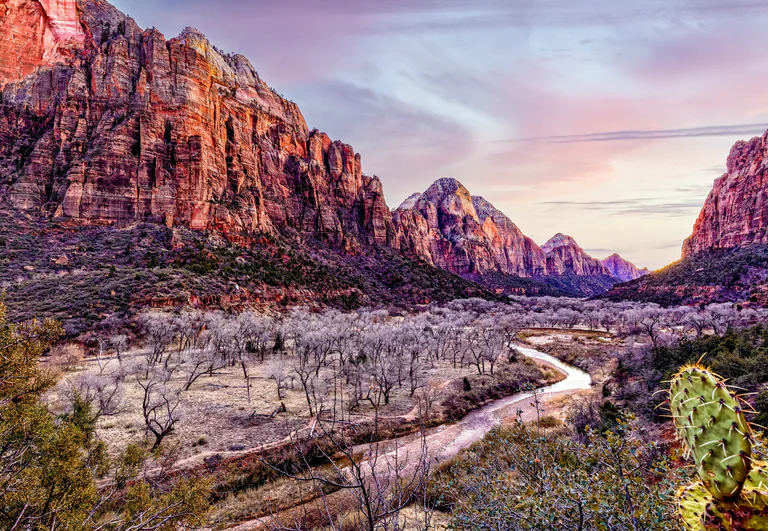 A winding river below steep canyon walls, with selective color in the red cliffs and sunset sky.