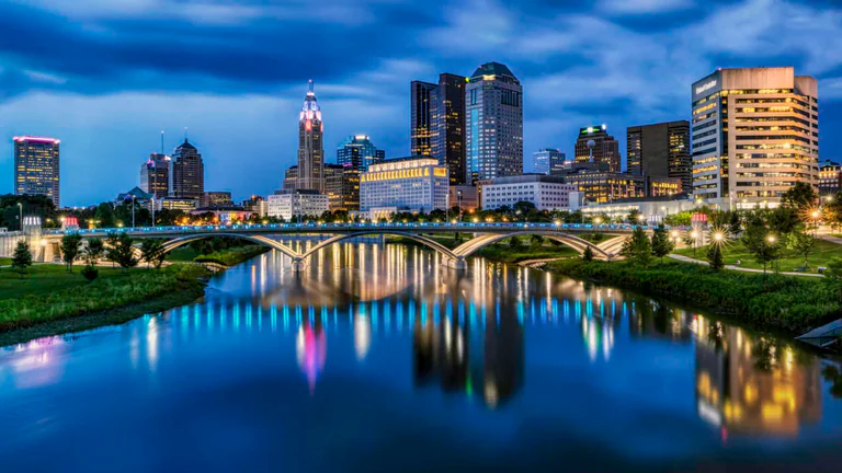Downtown Columbus and a river bridge reflected in blue water at dusk.