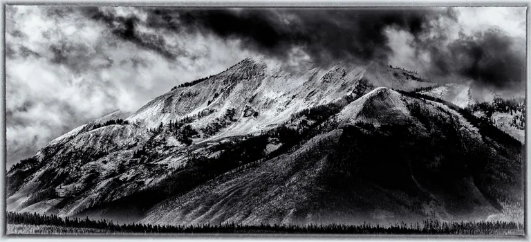Black-and-white mountain panorama with snow-covered slopes beneath heavy clouds.