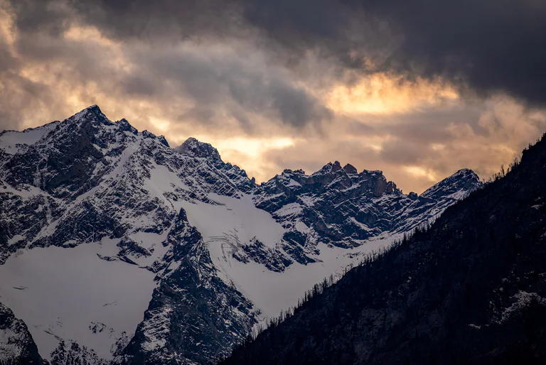 Jagged snow-covered mountains beneath a clouded sky touched by soft evening light.