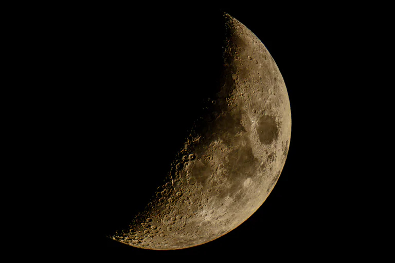 A partly illuminated Moon against a black sky, showing craters along its lit edge.