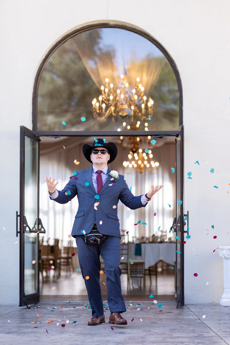 A person in a blue uniform holds a cap beneath a large arched entrance with a chandelier behind.