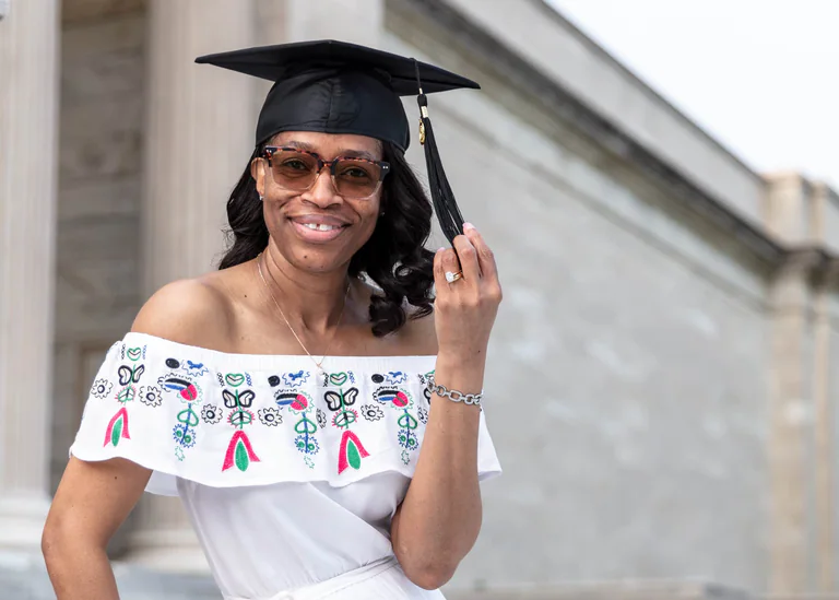Graduation portrait of a smiling woman wearing a black mortarboard and an embroidered white top.