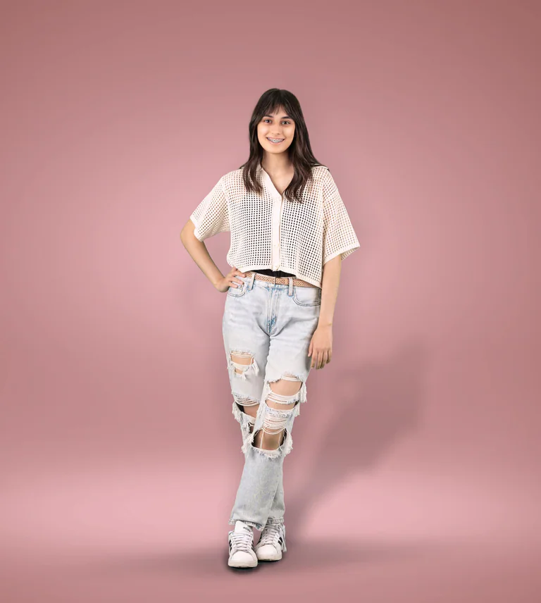 Full-length studio portrait of a woman in a white knitted top and light jeans against a pink background.