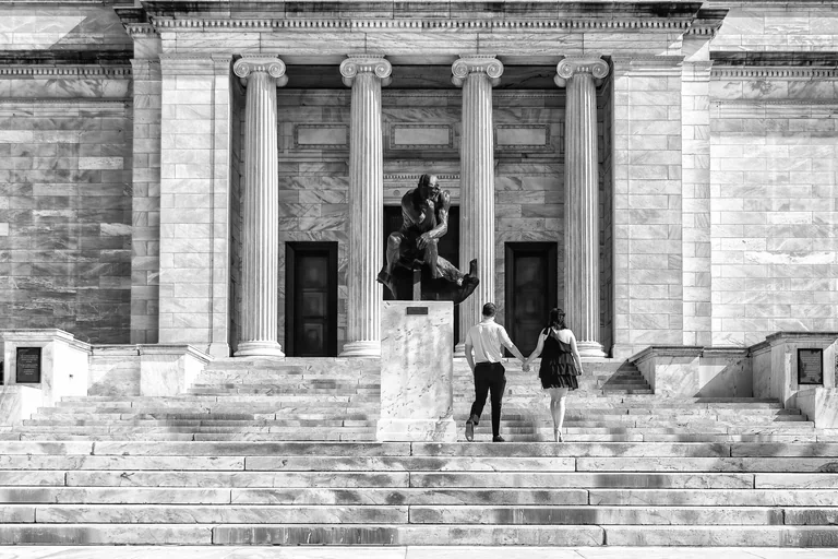 Black-and-white view of two people walking up broad steps toward a columned building.
