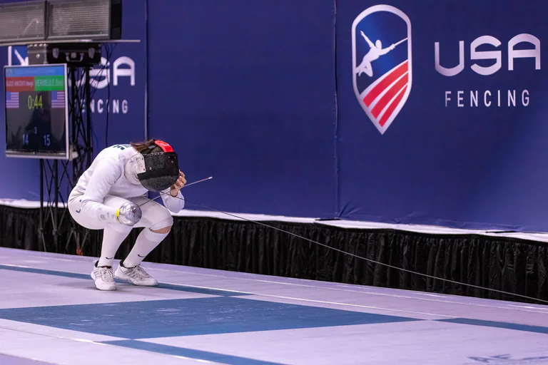 A masked fencer crouches alone at the edge of the piste.