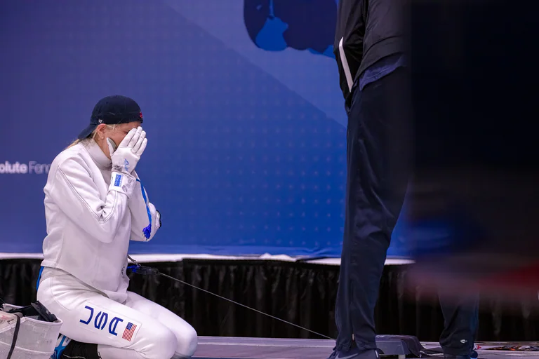 A fencer sits beside the piste with a towel pressed to the face.