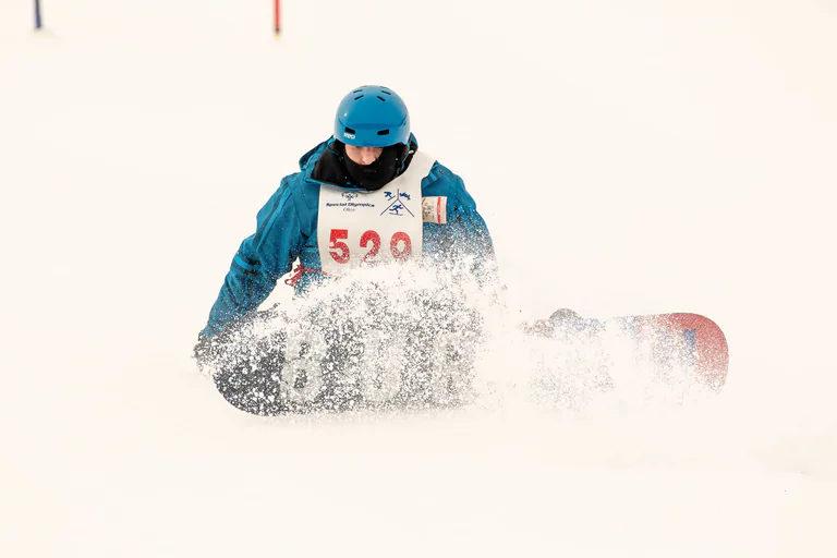 A snowboarder in a blue jacket turns through a spray of white snow.