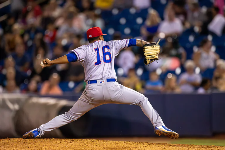 A pitcher in a white uniform stretches across the mound during a delivery.