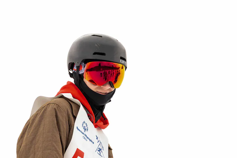 Close portrait of a snowboarder wearing a black helmet and mirrored red goggles.