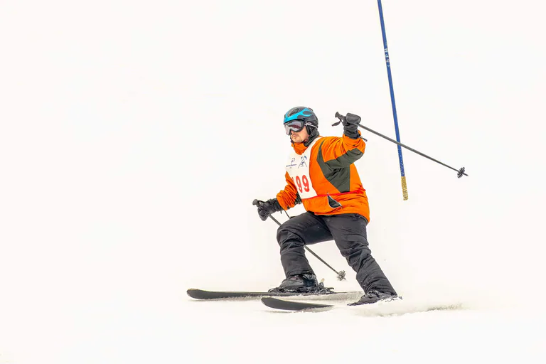 A skier in an orange bib descends between slalom gates with poles held wide.