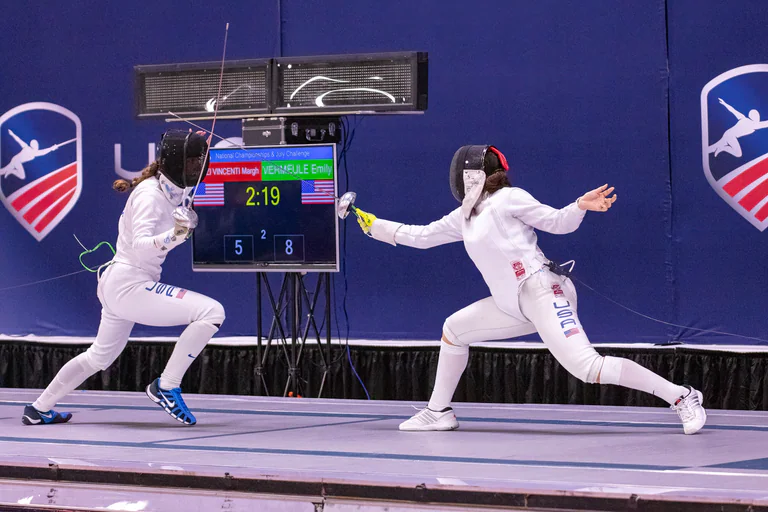 Two masked fencers face each other with blades extended across the piste.