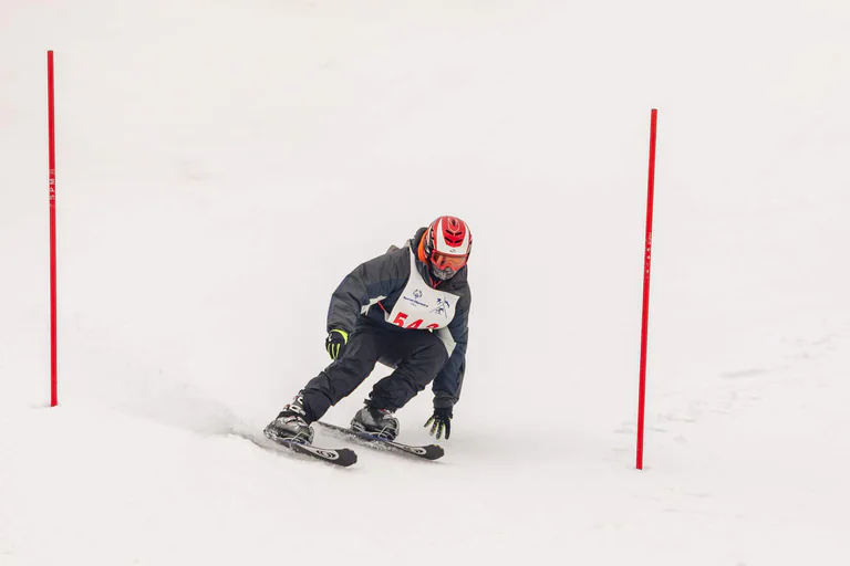 A skier in black leans sharply into a turn between red course markers.