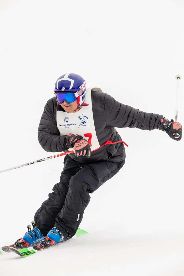 Close view of a blue-helmeted skier carving downhill with both poles in hand.