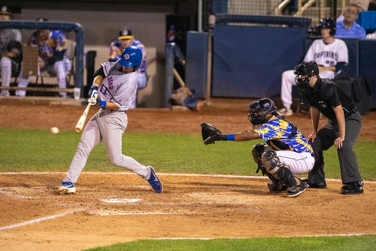 A batter in gray finishes a swing while the catcher reaches out behind.