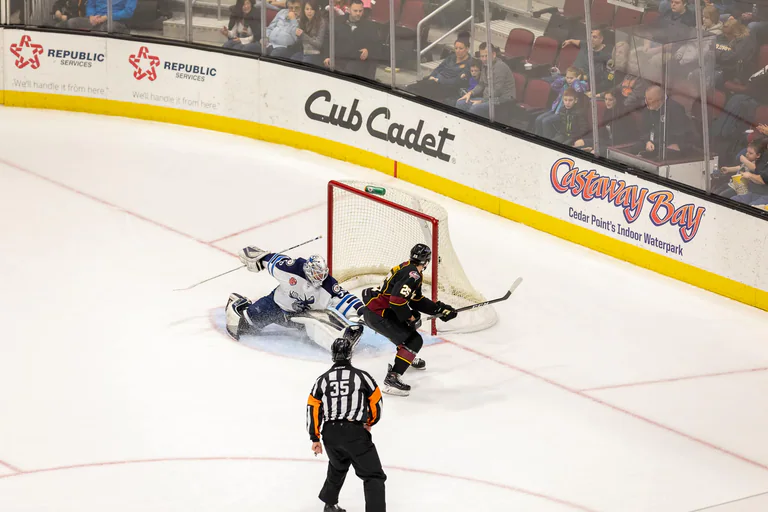 Players and a goaltender converge on the ice in front of the hockey goal.