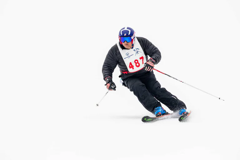 A skier in a blue helmet leans into a turn on a white slalom course.
