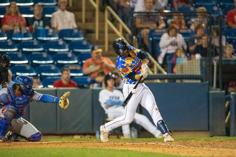 A batter bends low near home plate while the catcher reaches to receive a pitch.