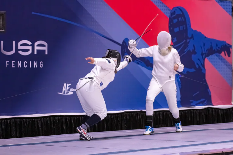 One fencer crouches into a low attack while an opponent extends a blade overhead.