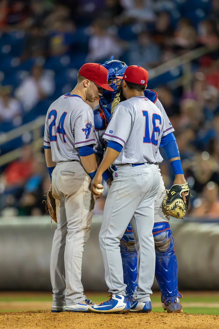 Baseball players gather on the mound in white and blue uniforms.