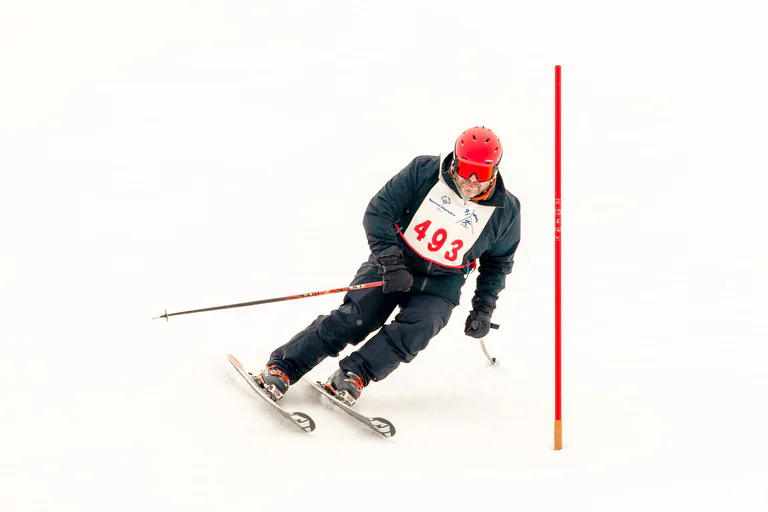 A skier in a red helmet carves a turn beside a red slalom pole.