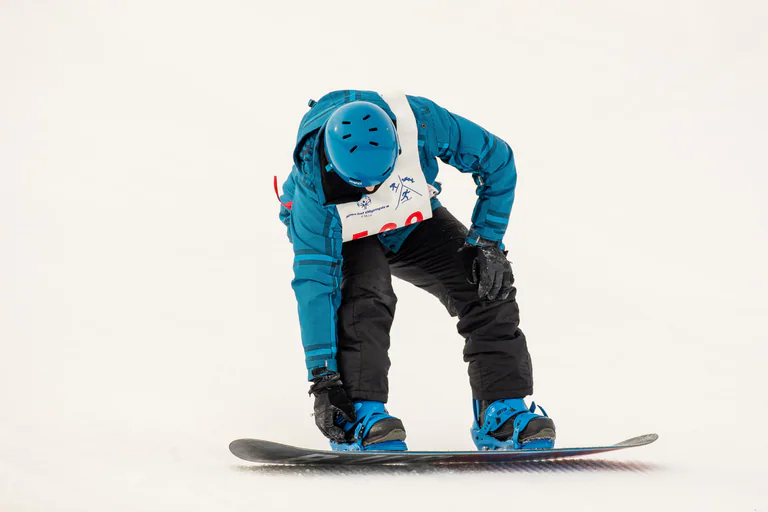 A snowboarder crouches over a board with one hand near the front binding.
