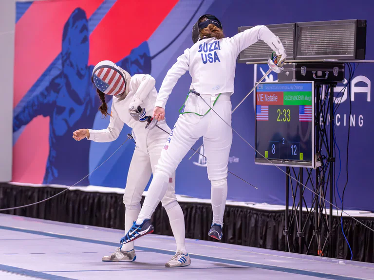 Two fencers meet at close range, one leaning forward as the other raises a blade.