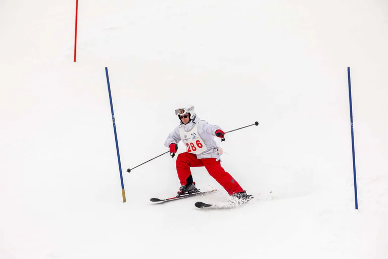 A skier in a white jacket and red trousers passes through a blue slalom gate.