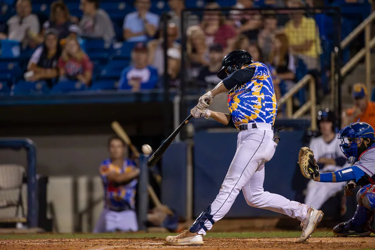 A batter in blue and yellow follows through on a swing at home plate.