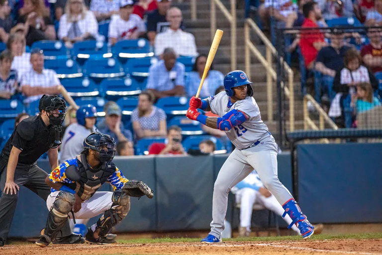 A batter waits with the bat raised while the catcher and umpire crouch behind home plate.