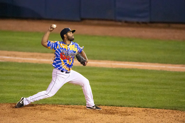 A pitcher in blue and yellow winds up to throw from the mound.